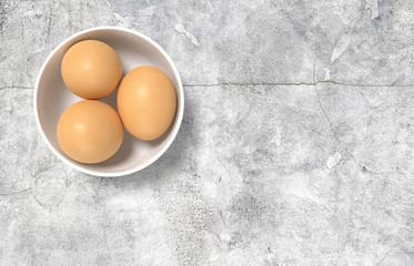Render of white ceramic bowl ful of eggs. Placed on concrete table.
