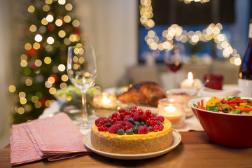 christmas dinner and eating concept - berry cake and other food on table at home