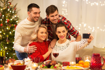 holidays and celebration concept - happy friends taking selfie by smartphone at home christmas dinner