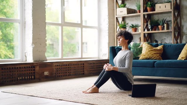 Yoga student is doing exercises and watching online lessons on laptop learning boat position sitting on floor. Internet, self-improvement and active youth concept.