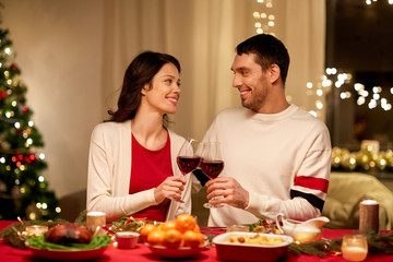 holidays, family and celebration concept - happy couple having christmas dinner at home and drinking red wine and clinking glasses