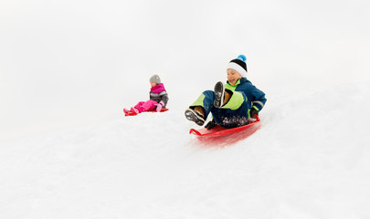 Fototapeta na wymiar childhood, sledging and season concept - happy little kids sliding on sleds down snow hill in winter