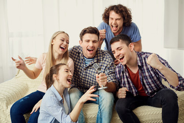 A group of friends with a microphone are singing fun songs at a party indoors.