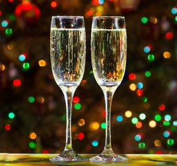 Christmas glasses with champagne on the background of the Christmas tree with toys decorated with colorful lights