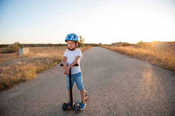 healthy dreaming little child with closed eyes in helmet with scooter on empty asphalt road
