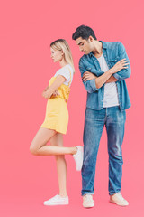 side view of angry woman standing with crossed arms and putting one leg on boyfriend while he looking down isolated on pink