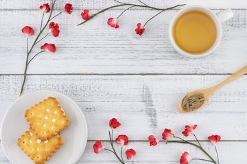 Tea, tea leaves on wooden spoon and biscuit decorate with red paper flowers on white wood background with copy space