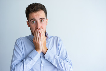 Shocked office worker feeling guilty. Young man with scared face covering mouth with both hands....