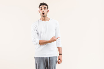 Fototapeta premium shocked young man looking at camera and pointing with finger at copy space isolated on beige