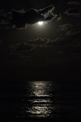 Full moon in a cloudy night sky reflecting moonlight on sea