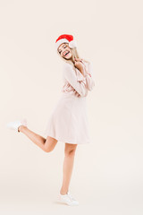 full length view of beautiful happy young woman in dress and santa hat isolated on beige