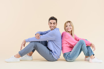 side view of happy young couple sitting back to back isolated on beige