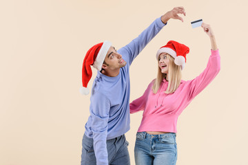 young couple in santa hats having fun with credit card isolated on beige
