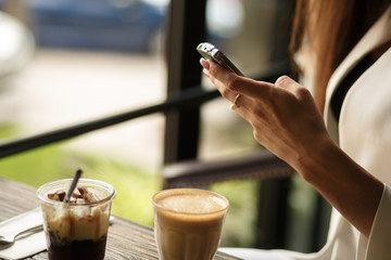 close up woman hands is chatting in the phone while sitting in a cafe with a cup of coffee and dessert