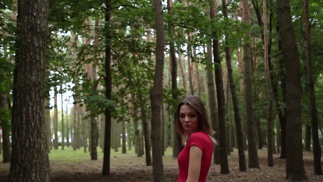A very beautiful and fashionable woman in a red dress walks through the forest.