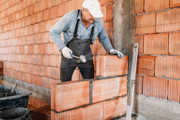 Worker installing bricks with mortar and rubber hammer. Construction industry details