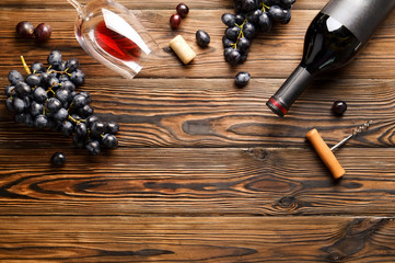 Vintage bottle of red wine with blank matte black label, corkscrew & bunches grapes on wooden table...