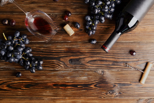 Vintage bottle of red wine with blank matte black label, corkscrew & bunches grapes on wooden table background. Expensive bottle of cabernet sauvignon concept. Copy space, top view, flat lay.