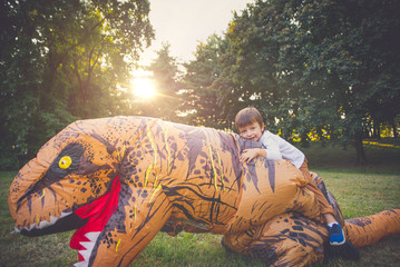 Father and son playing at the park, with a dinosaur costume, having fun with the family outdoor
