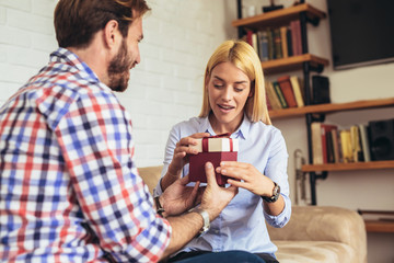 Smiling young man surprising cheerful woman with a gift box at home