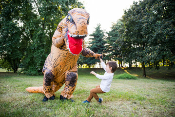 Father and son playing at the park, with a dinosaur costume, having fun with the family outdoor