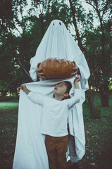 Father and son playing ghosts with white sheets in the garden, conceptual photos about halloween holidays