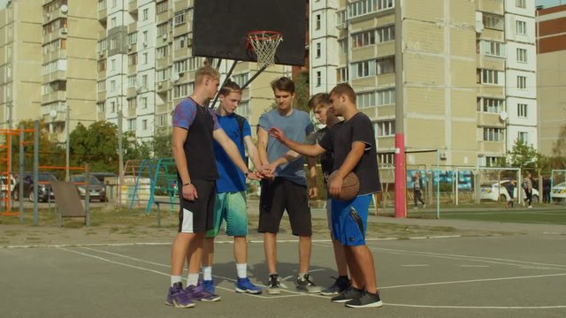 Teenage basketball team stacking hands on court before starting playing streetball game. Team of streetball playing making pile of hands, showing unity and willing to win basketball match outdoors.