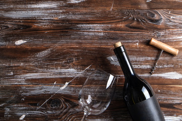 Vintage bottle of red wine with blank matte black label, corkscrew on grunged wooden table...