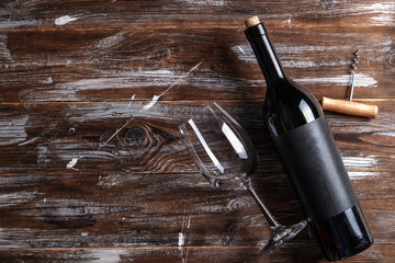 Vintage bottle of red wine with blank matte black label, corkscrew on grunged wooden table...