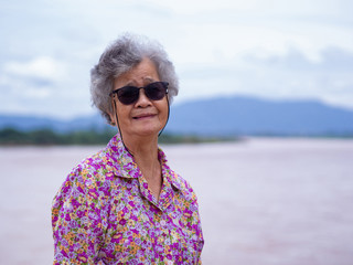 Portrait of elderly asian woman wearing sunglasses standing side the river.