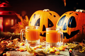 Halloween orange festive drink on vintage wooden autumn background with sweet corn, fallen leaves and straw, selective focus