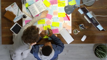 Top view of young black man and his female colleague discussing work using mind maps while generating ideas in office
