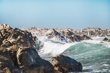 Dramatic crashing waves behind rocks on the shore.