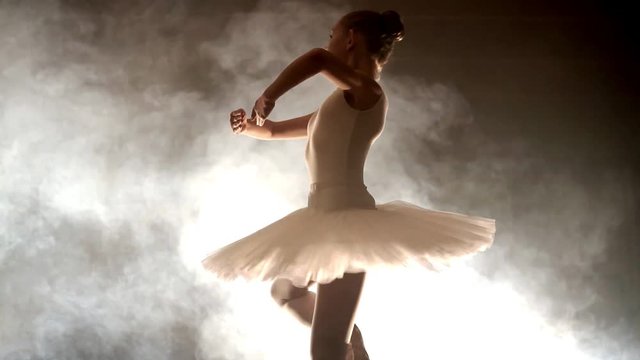 Ballerina dances on stage, close-up with magic light and smoke on the background.