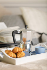 Breakfast in bed. On a white tray there is a coffee maker, coffee blue cup and croissants.