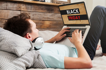 Man shopping on Black Friday special by the internet with a laptop computer, while lying down on...