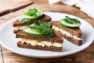 Sandwich with scrambled eggs, cucumbers and parsley on wooden rustic background.