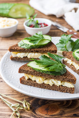 Sandwich with scrambled eggs, cucumbers and parsley on wooden rustic background.