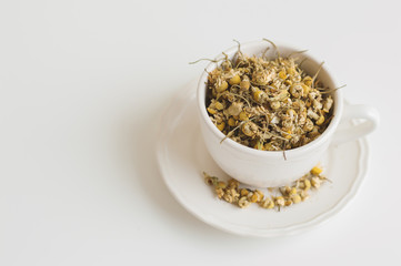Dried chamomile tea in a white cup. Camomile flowers. Healthy herbal drink on white table, dried...
