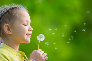 cute little girl blowing dandelion in the meadow