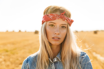 Portrait of cute woman 20s walking through golden field, during sunny day