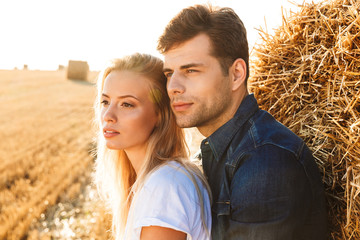 Image of people in love man and woman walking on golden field, and standing near big haystack