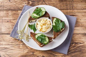 Sandwich with scrambled eggs, cucumbers and parsley on wooden rustic background.