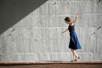 young girl posing against a concrete wall, dressed in black, hard light and shadows