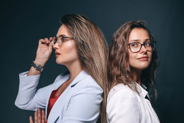 two beautiful sexy business women in in a jacket and glasses in the studio on a dark background. colleagues, partners - team.