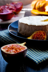 Camembert cheese on a black plate with figs, pistachios and wine in a glass, cut garnet on marble stone, fresh bread