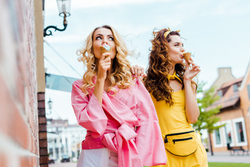 attractive young women in colorful clothes eating ice cream on street
