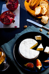 Camembert cheese on a black plate with figs, pistachios and wine in a glass, cut garnet on marble stone, fresh bread