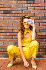 beautiful young woman in yellow clothes looking at camera through donut sitting in front of brick wall