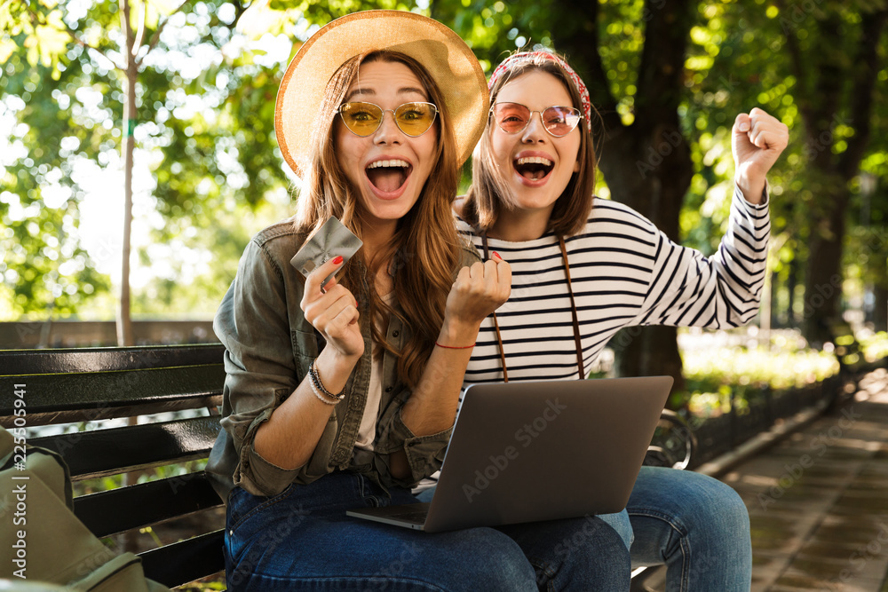 Canvas Prints Excited happy ladies friends outdoors sitting using laptop computer.